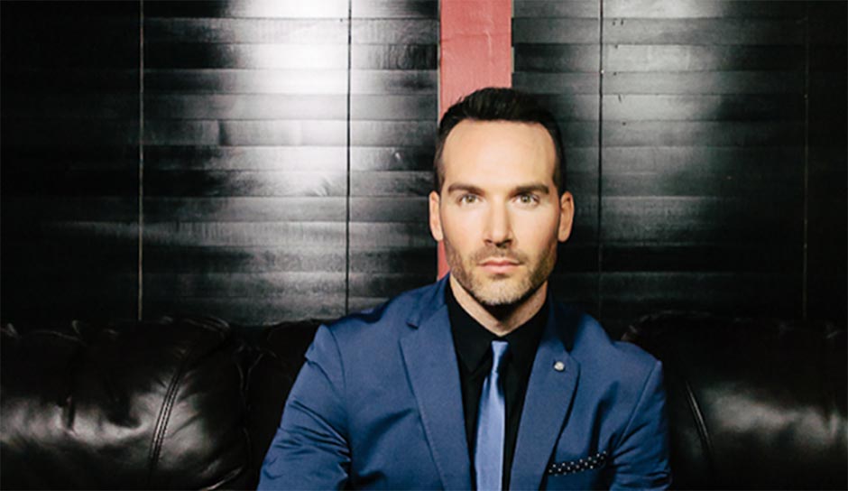 Man in a blue suit looking at the camera in front of a black wall